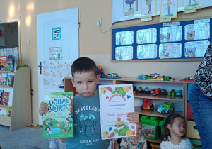 chłopiec pozuje do zdjęcia z dyplomem i książką