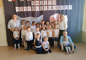 Dzieci i Panie pozują w strojach galowych na tle napisu 11 listopada