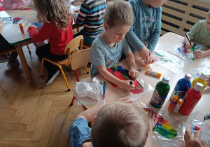 dzieci wykonują pracę plastyczną z wykorzystaniem farb