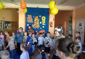 seniorzy w przebrania wspólnie z dziećmi tańczą w kole