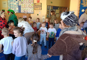 seniorzy w przebrania wspólnie z dziećmi tańczą w kole