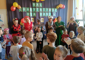 seniorzy w przebrania wspólnie z dziećmi tańczą w kole