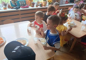 dzieci siedzą przy stolikach i jedzą popcorn