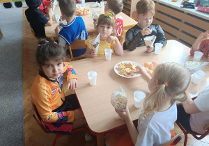 dzieci siedzą przy stolikach i jedzą popcorn