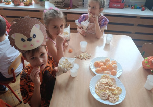 dzieci siedzą przy stolikach i jedzą popcorn