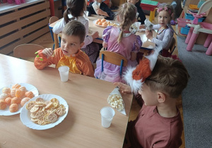 dzieci siedzą przy stolikach i jedzą popcorn