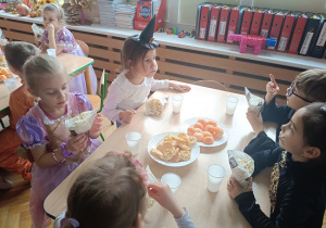 dzieci siedzą przy stolikach i jedzą popcorn