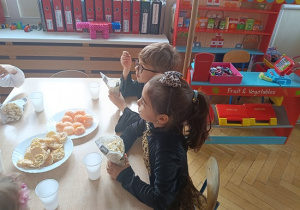 dzieci siedzą przy stolikach i jedzą popcorn