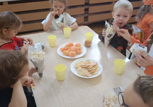 dzieci siedzą przy stolikach i jedzą popcorn