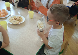 dzieci siedzą przy stolikach i jedzą popcorn