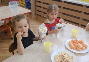 dzieci siedzą przy stolikach i jedzą popcorn