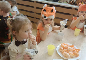 dzieci siedzą przy stolikach i jedzą popcorn