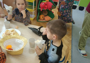 dzieci siedzą przy stolikach i jedzą popcorn