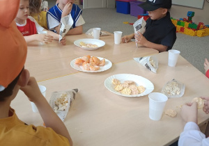 dzieci siedzą przy stolikach i jedzą popcorn