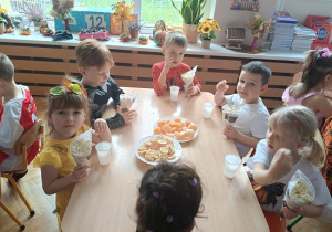 dzieci siedzą przy stole i jedzą popcorn