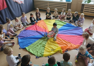 chłopiec siedzi na kolorowej chuście z torbą cukierków wokół niego siedzi grupa dzieci