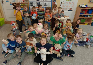 dzieci siedzą na dywanie i prezentują swoje pluszowe misie