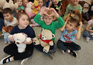 dzieci siedzą na dywanie i prezentują swoje pluszowe misie