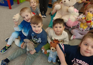 dzieci siedzą na dywanie i prezentują swoje pluszowe misie