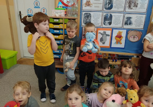 dzieci siedzą na dywanie i prezentują swoje pluszowe misie