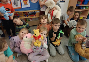 dzieci siedzą na dywanie i prezentują swoje pluszowe misie