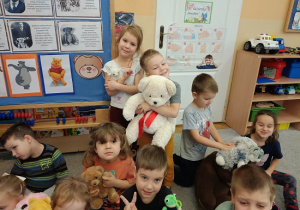 dzieci siedzą na dywanie i prezentują swoje pluszowe misie