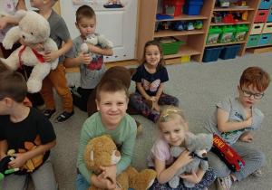 dzieci siedzą na dywanie i prezentują swoje pluszowe misie