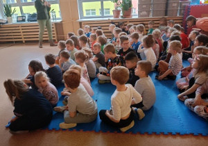 dzieci siedzą na materacu i słuchają Pani leśnik