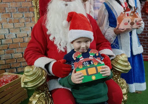 chłopiec z prezentem w obecności Mikołaja i śnieżynki