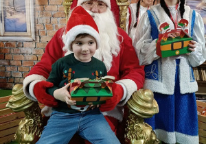 chłopiec z prezentem w obecności Mikołaja i śnieżynki