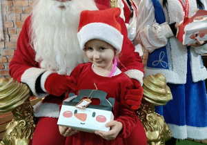 dziewczynka z prezentem w obecności Mikołaja i Śnieżynki