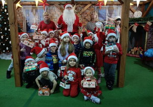 dzieci z prezentami w czapkach mikołajkowych w obecności Mikołaja