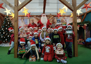 dzieci z prezentami w czapkach mikołajkowych w obecności Mikołaja