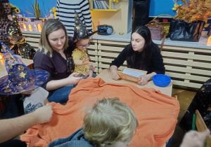 dzieci wspólnie z mamami losują różne przedmioty spod koca