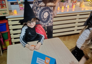 chłopiec w stroju czarodzieja siedzi przy stoliku z miską wody