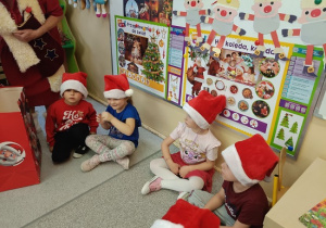 dzieci w mikołajkowych czapkach siedzą przy tablicy