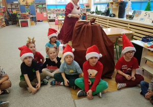 dzieci w czapkach mikołajkowych siedzą przy worku pełnym prezentów