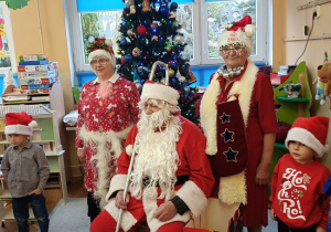 mMikołaj, śnieżynki i dzieci stoją przy choince