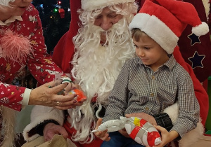chłopiec z prezentem siedzi na kolanach Mikołaja