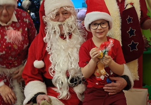 chłopiec z prezentem siedzi na kolanach Mikołaja