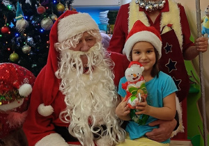 dziewczynka z prezentem w rękach siedzi na kolanach u Mikołaja