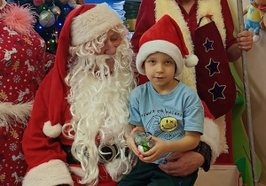 chłopiec z prezentem siedzi na kolanach Mikołaja