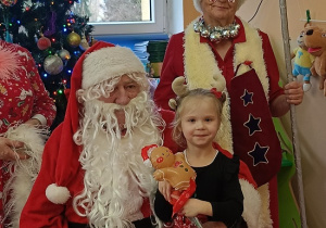 dziewczynka z prezentem w rękach siedzi na kolanach u Mikołaja