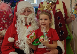 dziewczynka z prezentem w rękach siedzi na kolanach u Mikołaja