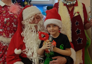 chłopiec z prezentem siedzi na kolanach Mikołaja