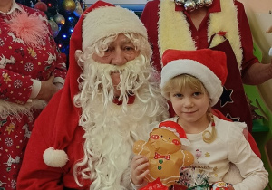 dziewczynka z prezentem w rękach siedzi na kolanach u Mikołaja