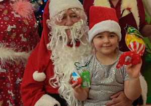 dziewczynka z prezentem w rękach siedzi na kolanach u Mikołaja