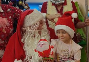 dziewczynka z prezentem w rękach siedzi na kolanach u Mikołaja