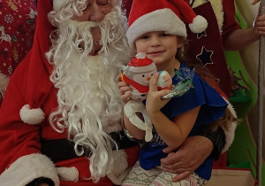 dziewczynka z prezentem w rękach siedzi na kolanach u Mikołaja