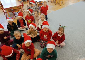 dzieci w czapkach mikołajkowych siedzą na wykładzinie
